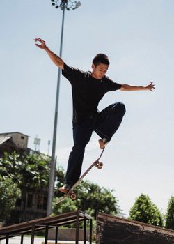 一名亚洲男子在阳光明媚的城市公园里，展示了令人印象深刻的滑板技巧