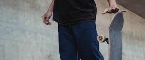 Free Crop anonymous male in casual outfit standing with skateboard near gray concrete wall Stock Photo