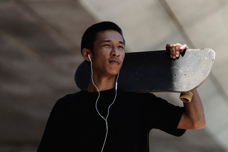 Young Asian Man With Earphones And Skateboard