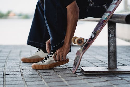 牛仔布感人的运动鞋的滑板在混凝土砖附近的滑板的人