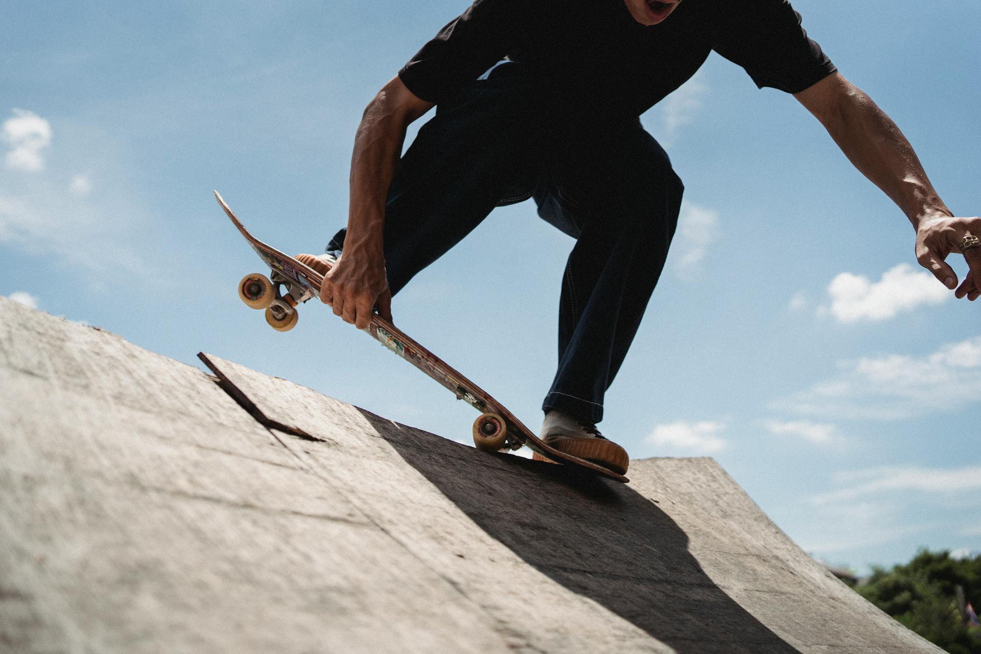 Crop anonymous male in casual outfit performing trick on skateboard on edge of ramp on sunny day