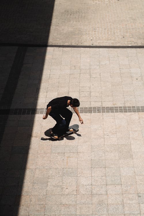 From above of young slim male moving on skateboard on concrete tile on sunny day