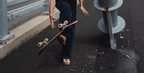 Crop anonymous male in casual outfit showing trick with skateboard on street of town