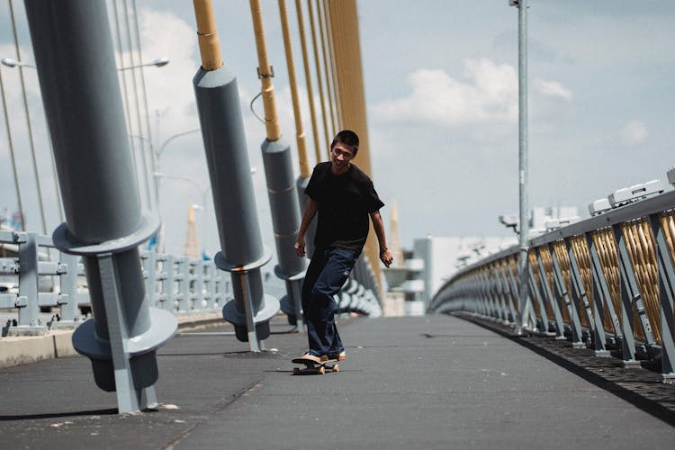 Asian Man Riding Skateboard On Bridge