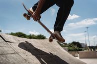 Crop anonymous male in sneakers performing trick on skateboard in skate park during sunny day