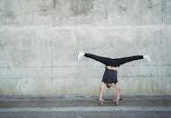 Anonymous guy in activewear doing handstand on skateboard while riding alone near concrete wall and pavement