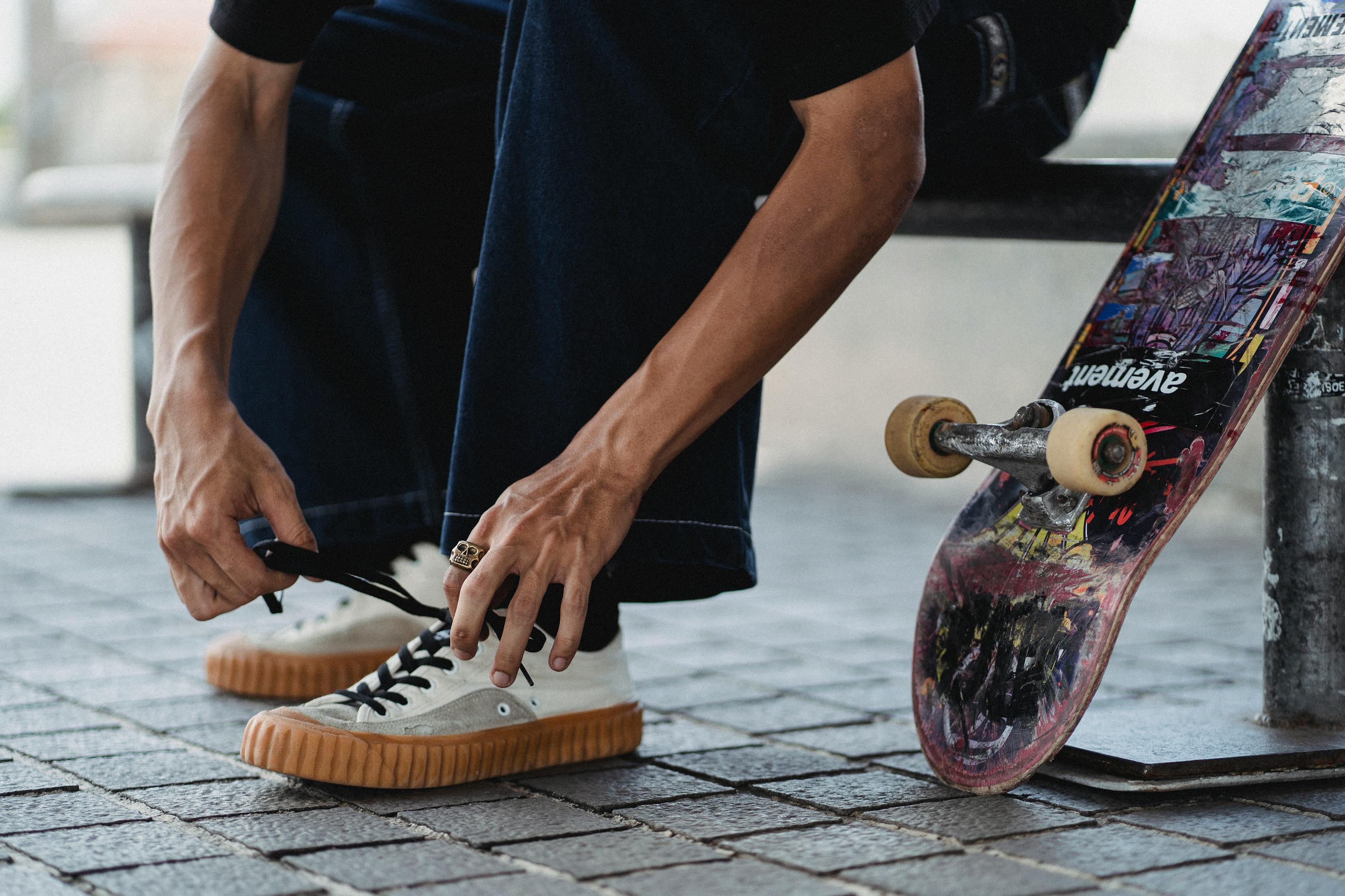 Crop young man tying shoelaces on white sneakers near skateboard · Free ...