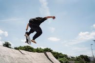 夏日阳光明媚，一位年轻人在城市公园的旧坡道上表演高奥利特技，留下背影