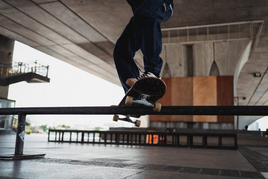 Free Unrecognizable skater doing grind trick on rail in skater training area Stock Photo
