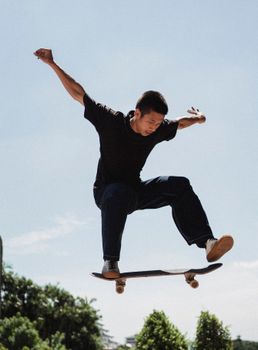 夏日里，坚定的亚洲人在公园里踩着滑板，在蓝天下高高跃起