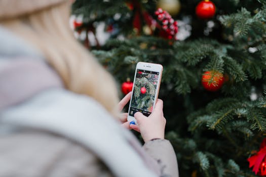 A person captures a photo of a decorated Christmas tree using a smartphone outdoors.