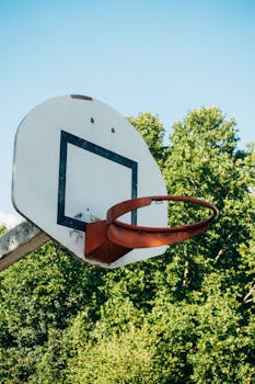 A basketball hoop mounted on a backboard against a clear blue sky and green trees.