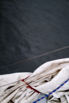 Close-up of boat sails with raindrops creating patterns on the water's surface below.