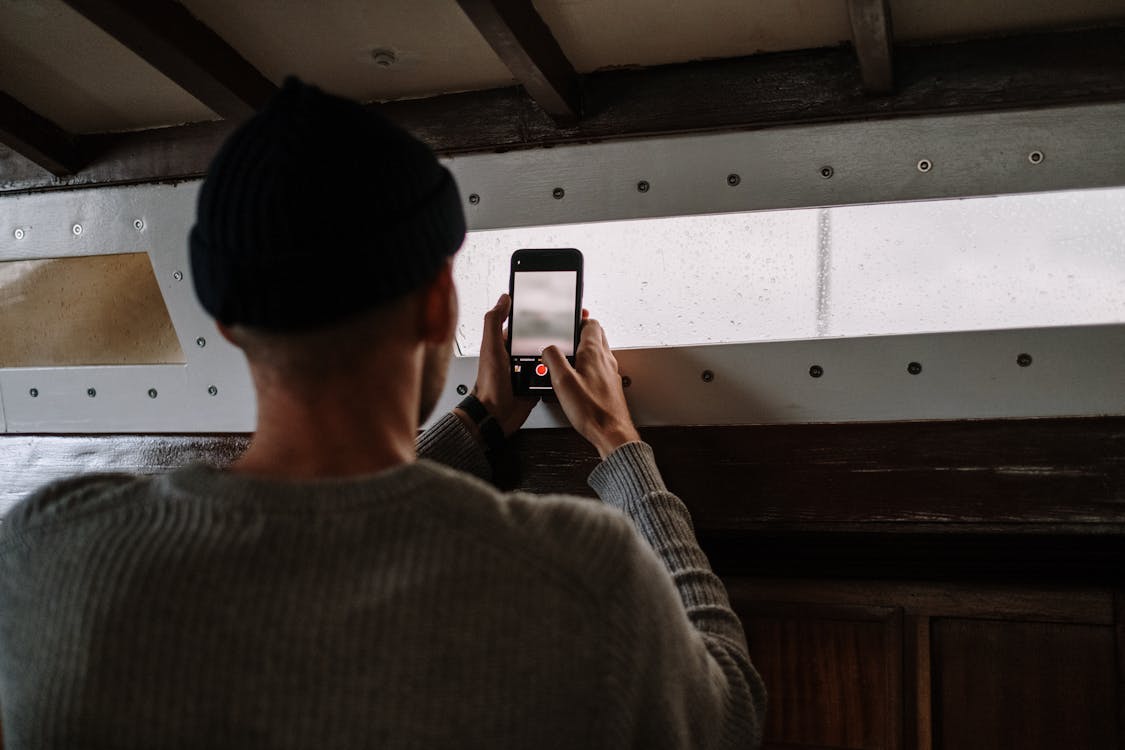 Free Man in Gray Sweater Taking Photo Using a Smartphone Stock Photo