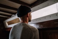 雨天，一个戴着无檐帽的男子沉思着望向窗外，营造出一种忧郁的氛围