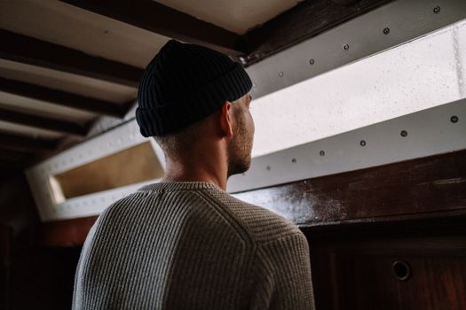 雨天，一个戴着无檐帽的男子沉思着望向窗外，营造出一种忧郁的氛围