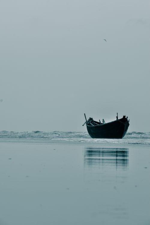 Free A solitary fishing boat rests on the tranquil waters of Mandarmani beach at dawn. Stock Photo