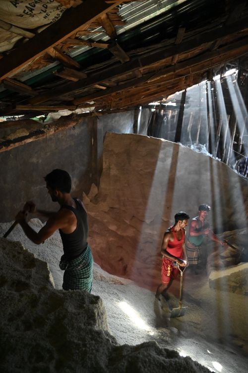 Free Three men working in a sand mine with sunbeams illuminating the indoor setting in Chattogram, Bangladesh. Stock Photo