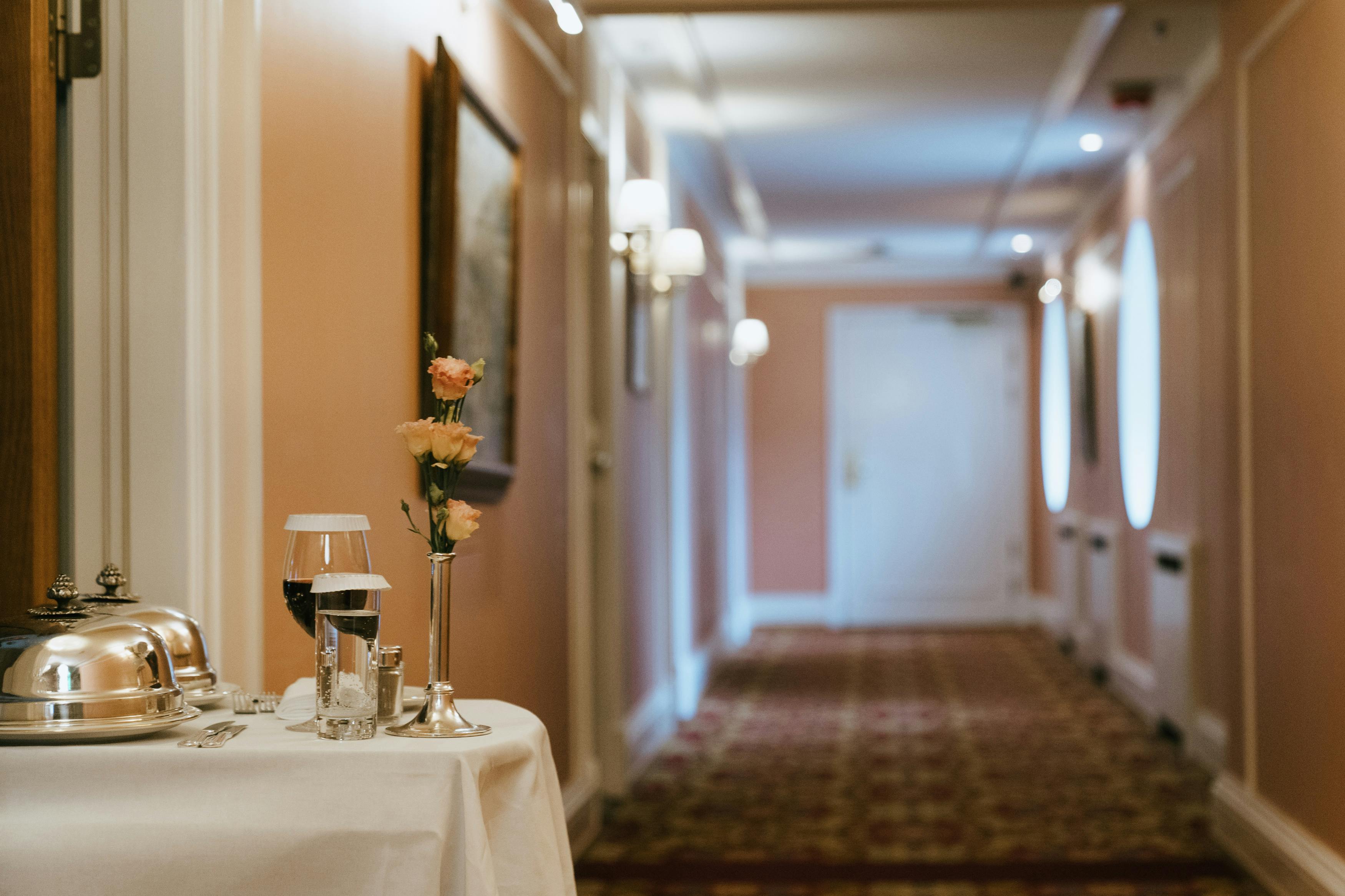 A luxurious hotel corridor featuring a room service table with flowers and wine, creating a warm ambiance.