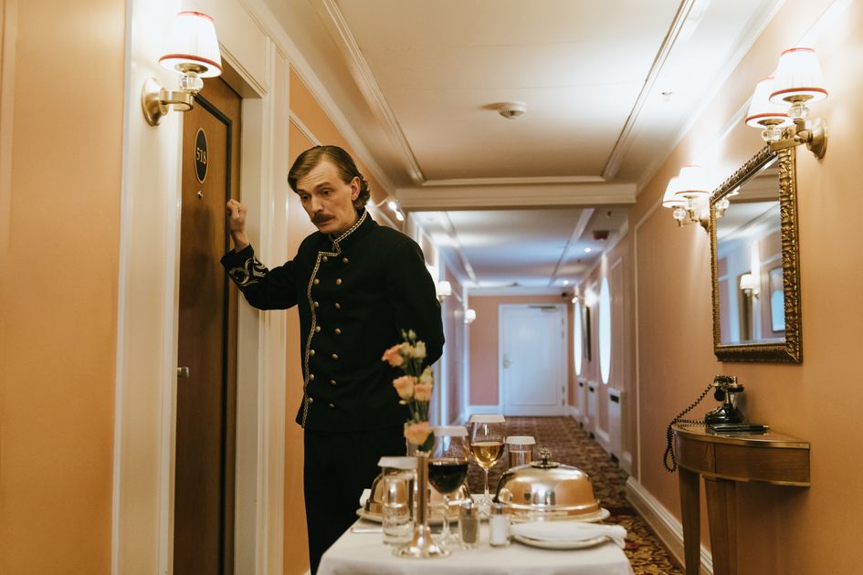 A hotel staff member in uniform serves room service with a trolley in a luxurious hallway. Related image for hotel operations in Global hotels.