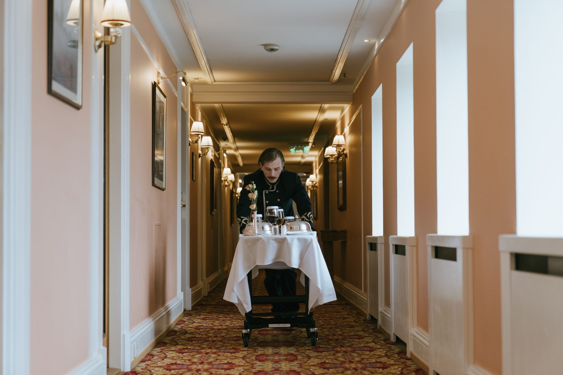 Behind-the-scenes hospitality — a hotel attendant preparing a service trolley in a warmly lit corridor before guest arrivals