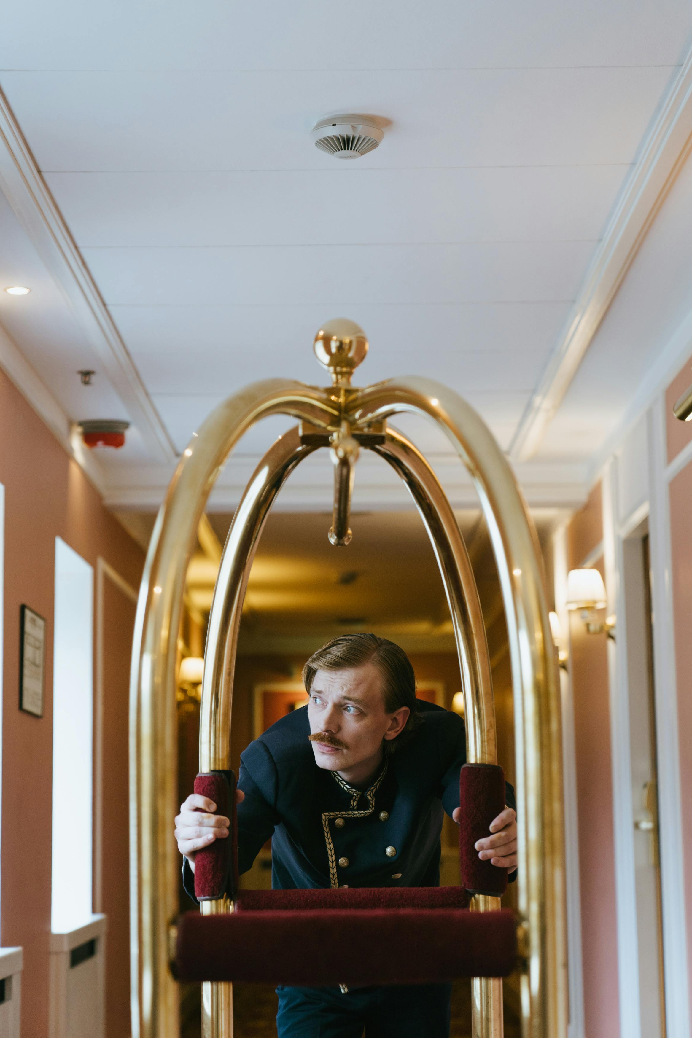 Uniformed hotel porter pushing a luggage trolley in a luxurious corridor, showcasing hospitality.
