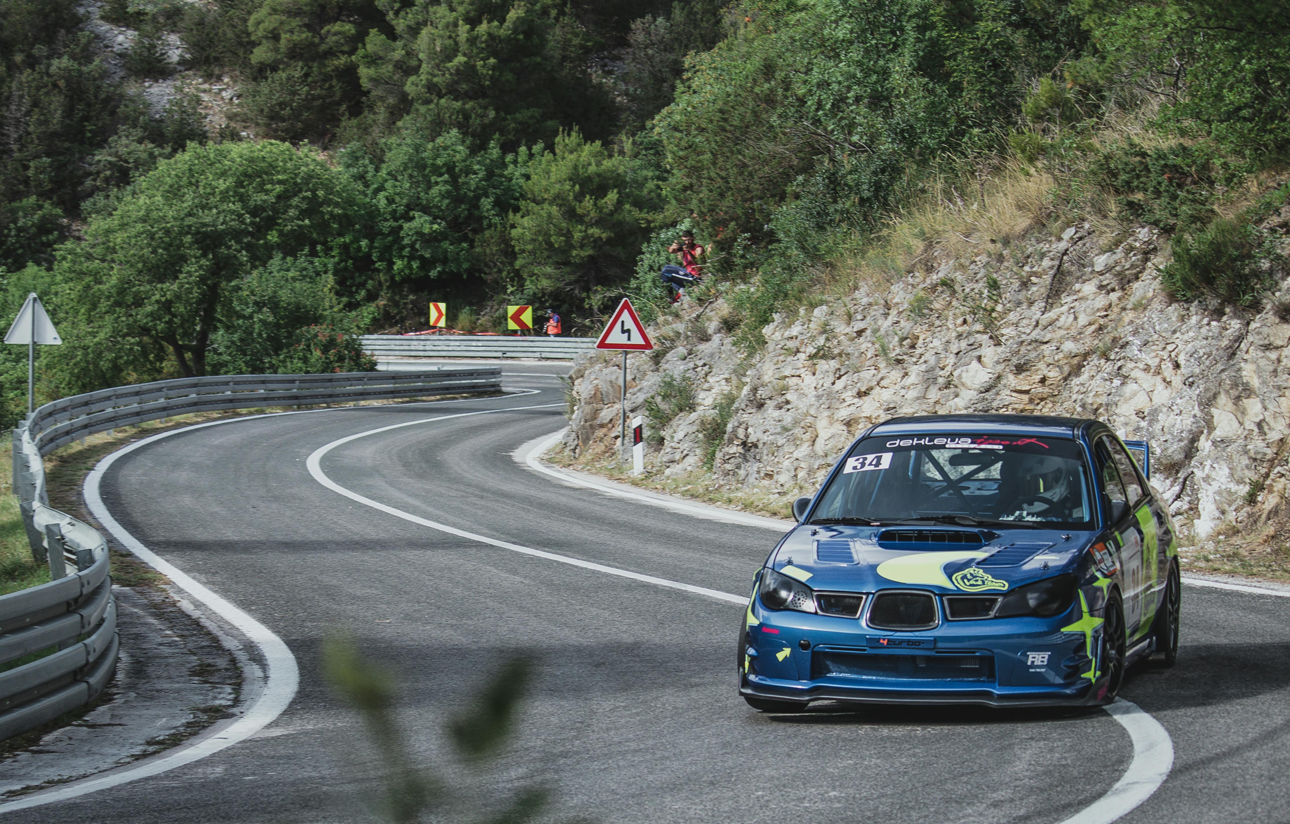 Free Subaru WRX race car speeding on a winding mountain road with lush greenery, showcasing thrilling motorsport action. Stock Photo