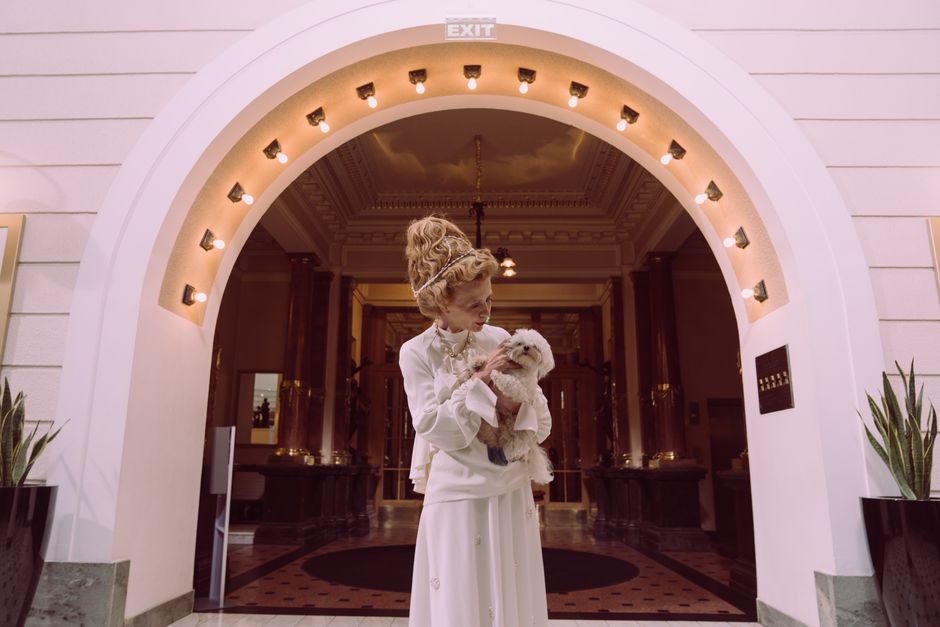 luxury dog boarding amenities The Woodlands - A senior woman elegantly dressed, holding a small dog in a luxurious hotel lobby.