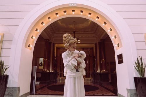 Free A senior woman elegantly dressed, holding a small dog in a luxurious hotel lobby. Stock Photo