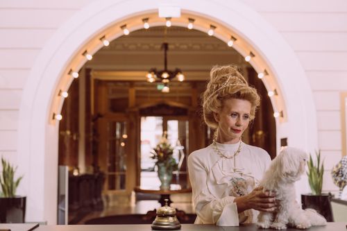 Free An elegant woman holding a dog at a luxurious hotel reception desk. Stock Photo