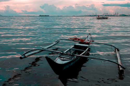 Free A beautiful outrigger boat floats on calm waters during a stunning sunset, perfect for travel inspiration. Stock Photo