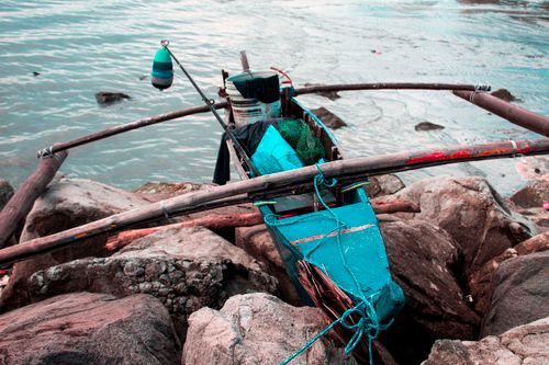 Free Colorful fishing boat docked on rocky seashore with ropes and nets, ready for adventure. Stock Photo