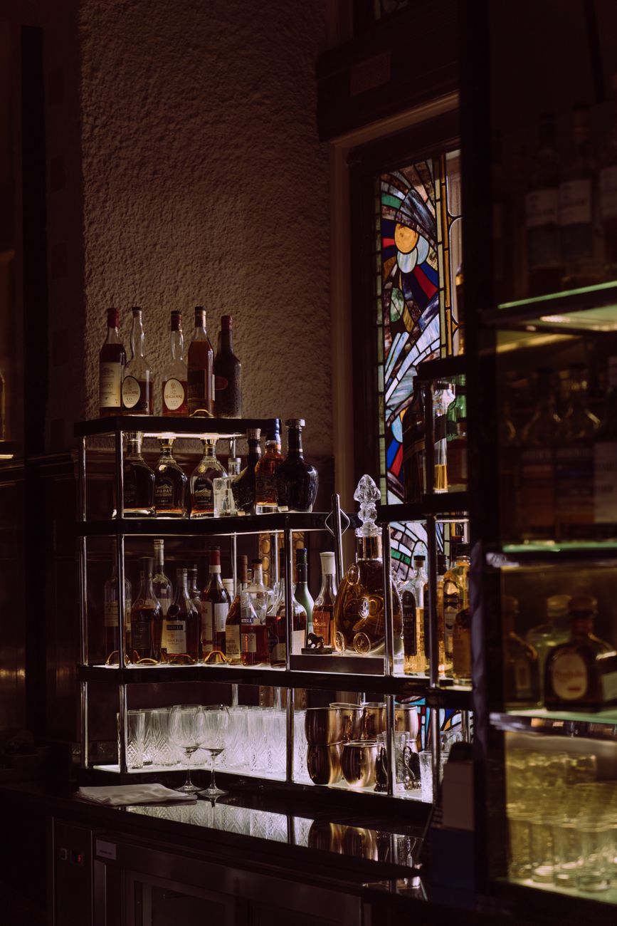 An atmospheric bar scene showcasing a variety of liquor bottles on display with stained glass backdrop.