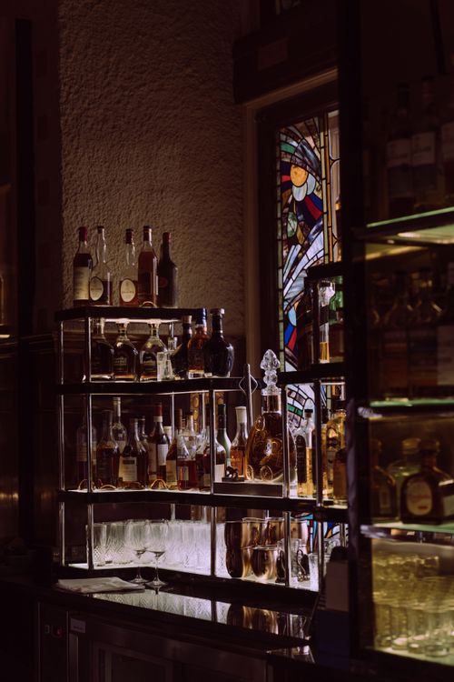 Free An atmospheric bar scene showcasing a variety of liquor bottles on display with stained glass backdrop. Stock Photo