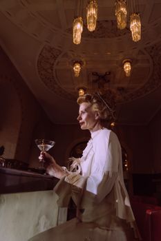 A woman in vintage attire enjoys a cocktail in a classy, luxurious bar setting.