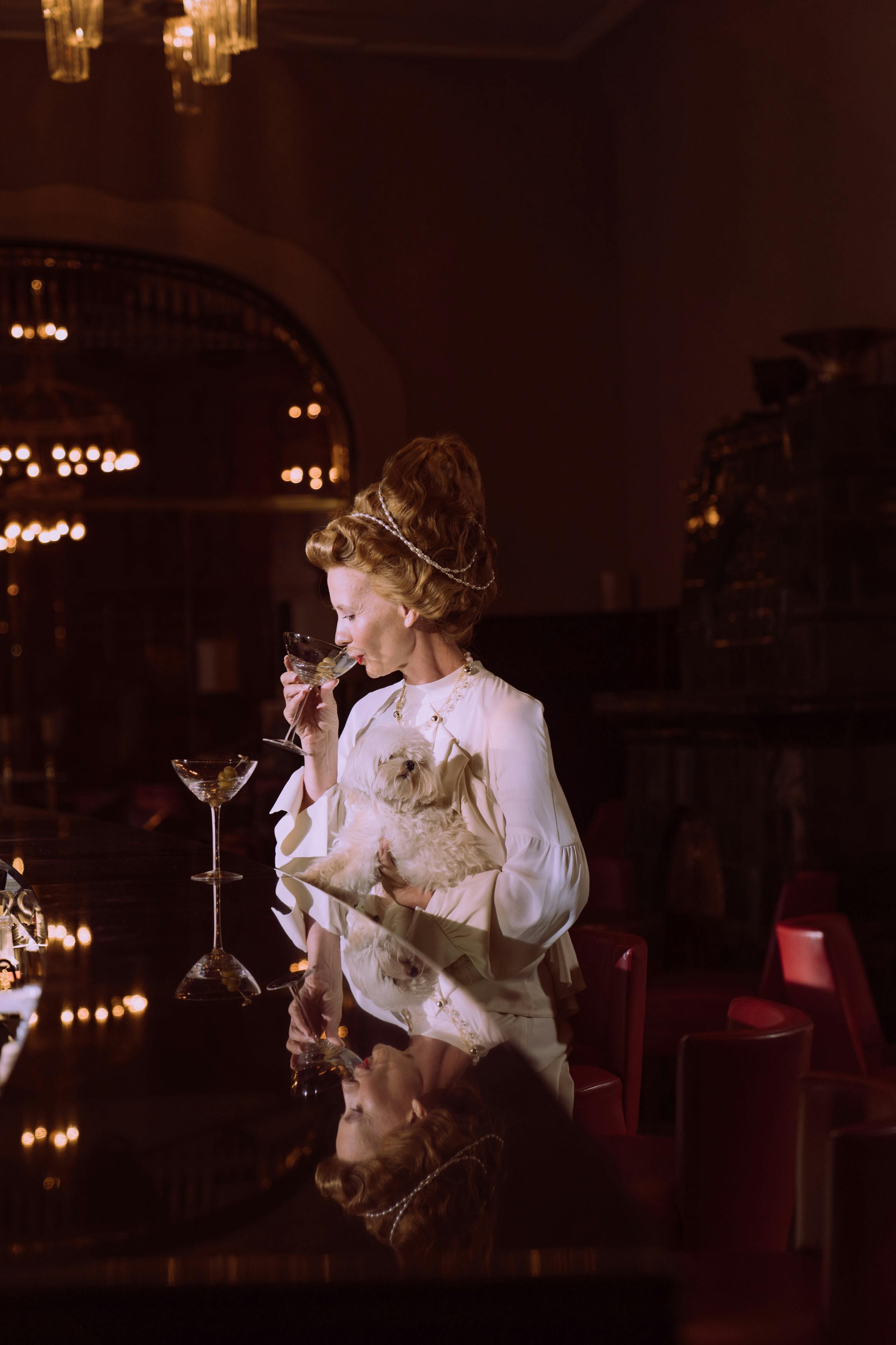 一位穿着优雅的女士带着她的马耳他狗，在豪华的酒吧里喝酒