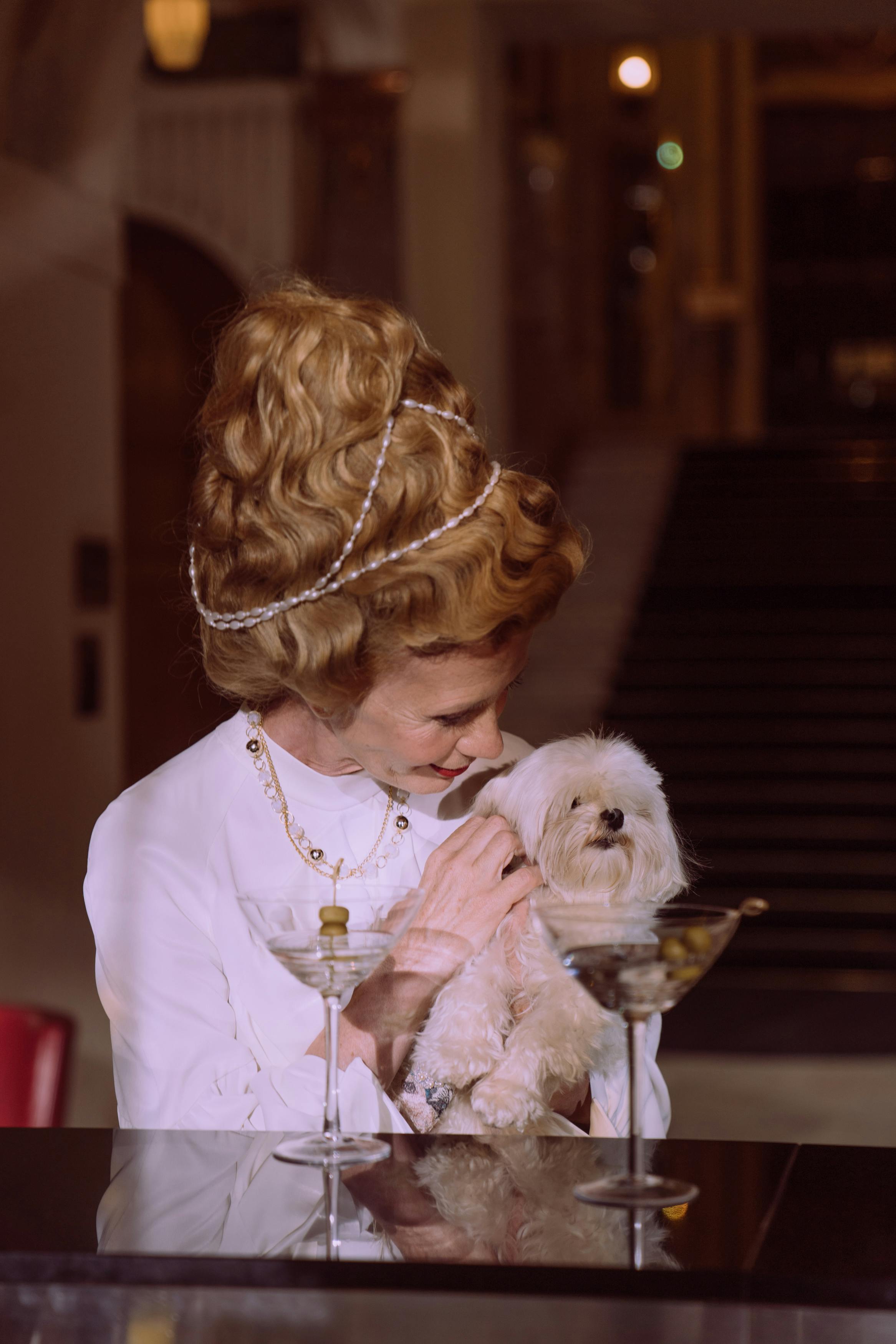 woman in white long sleeve shirt carrying white long coated small dog