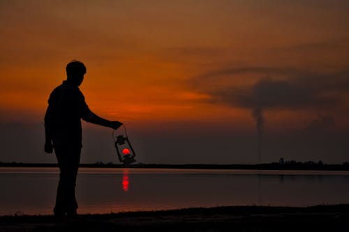 Free Silhouette of man with oil lamp on shore at sunset Stock Photo