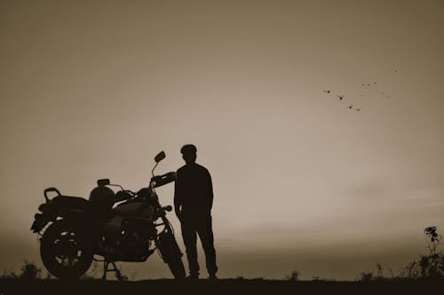 Black and white full body silhouette of anonymous biker with motorcycle enjoying freedom in solitude