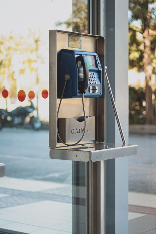 Free A modern public telephone booth with a blue telephone, set in a sunny indoor environment. Stock Photo