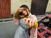 From above of young serious female in trendy outfit while standing near old damaged car