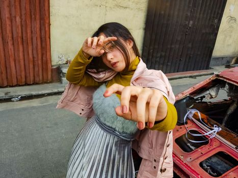 一位穿着时髦、神情严肃的年轻女性站在一辆破旧的汽车旁，从上方俯视