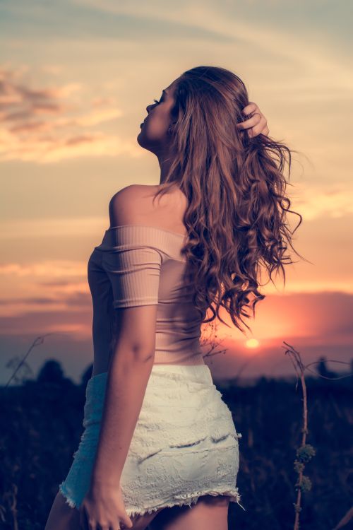 Free A woman enjoying a peaceful moment in a field at sunset, her hand in her hair, embracing nature. Stock Photo