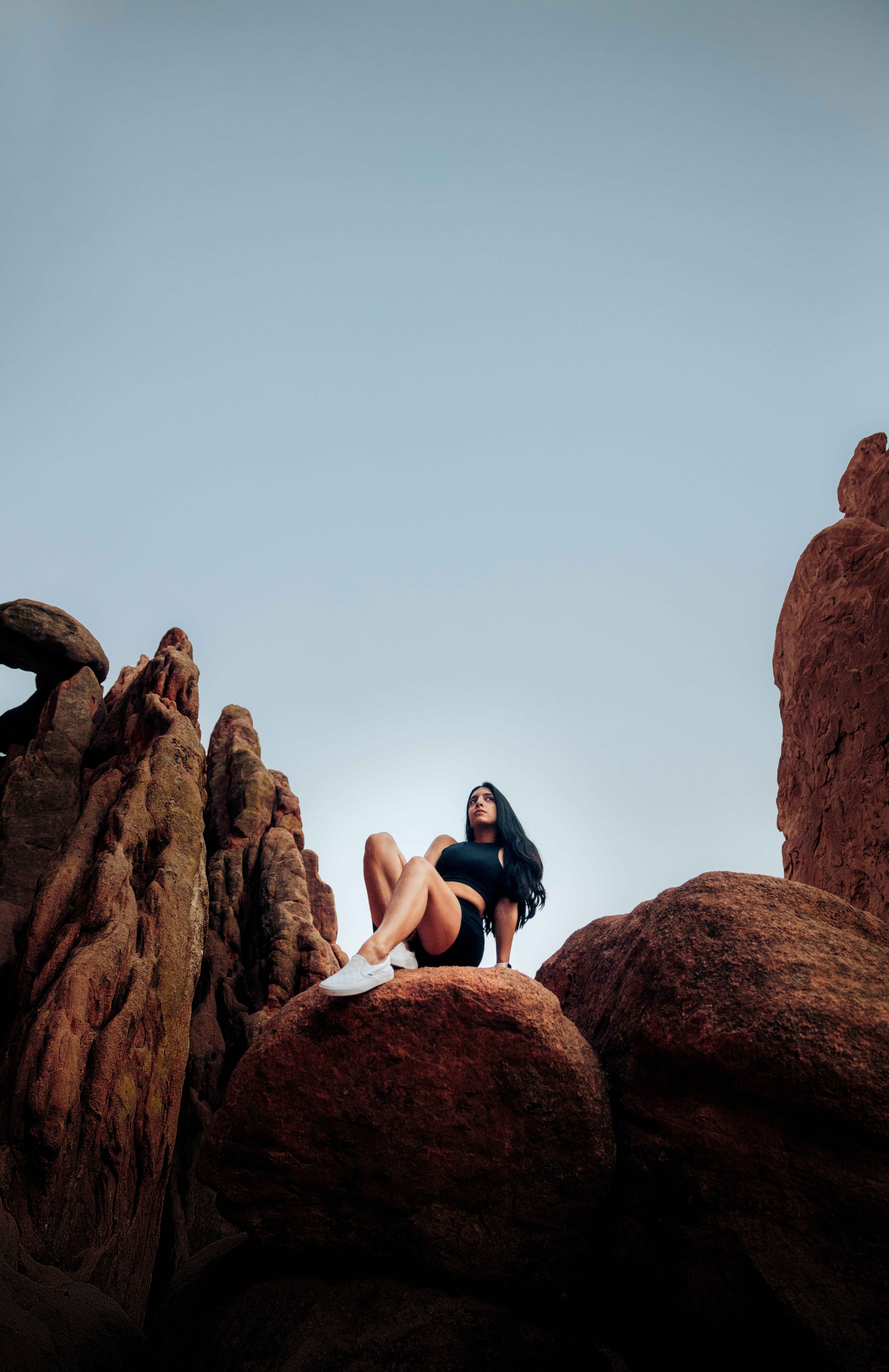 woman in black crop top and black shorts sitting on brown rock formation