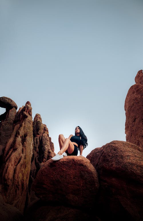 茶色の岩層に座っている黒いクロップトップと黒いショートパンツの女性