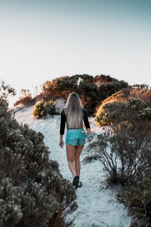 A Person in Black Long Sleeve Shirt and Denim Shorts Walking on White Sand