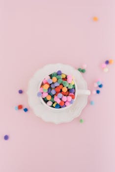 瓷杯中放着迷人的彩色弹球，背景是柔和的粉色，非常适合创意设计