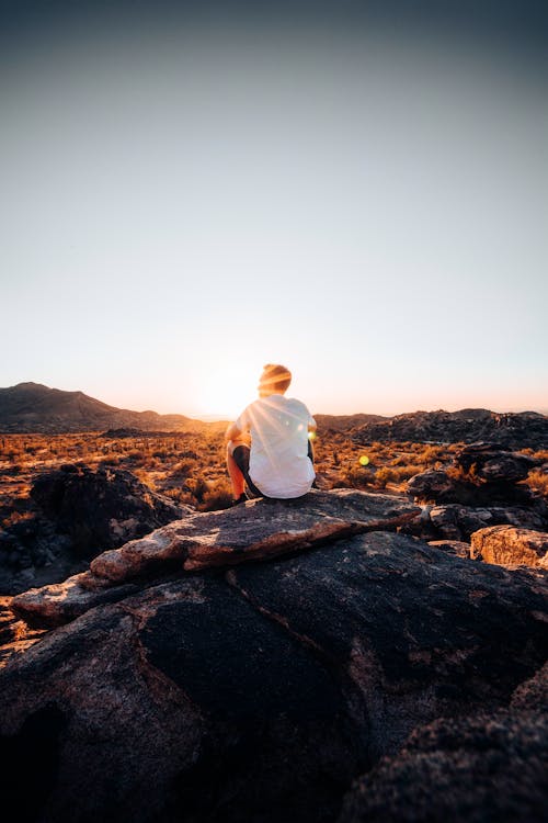 Free A Person in White Shirt Sitting on Brown Rock Against the Sun Stock Photo