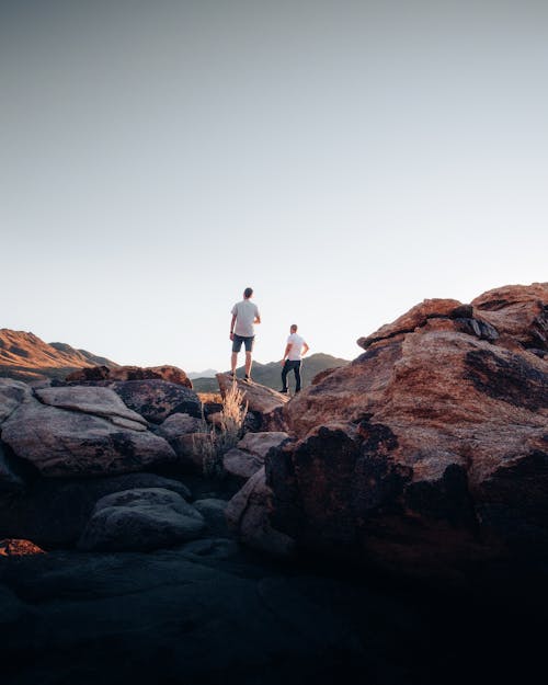 Two Men Standing on  Brown Rocks