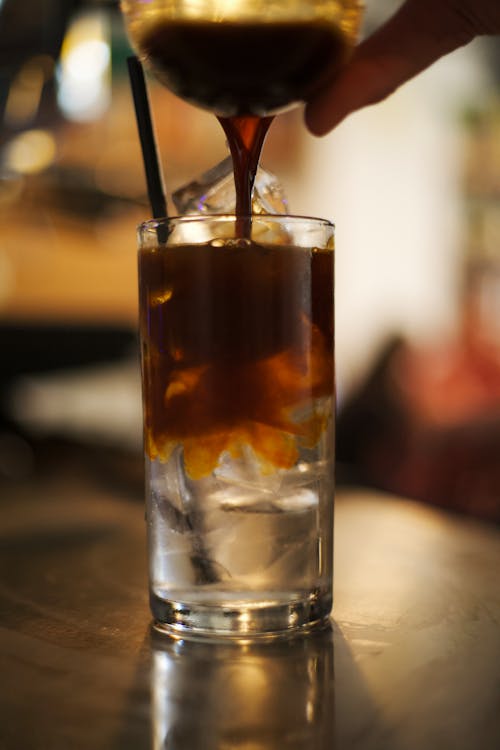 Pouring Brown Liquid on a Clear Drinking Glass